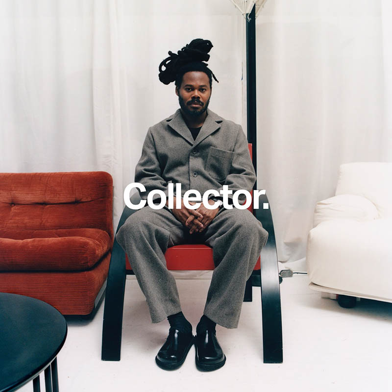 Man with dreadlocks in a grey suit seated on a red chair between red and white sofas, bold 'Collector.' text overlay