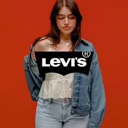 Giovane donna con top chiaro e jeans che si sta togliendo parzialmente una giacca di denim blu, in piedi davanti a uno sfondo arancione solido, occhi chiusi.