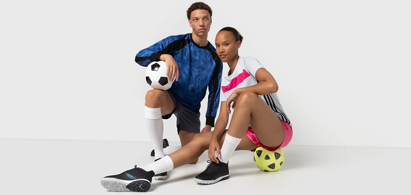 Due atleti in abbigliamento sportivo posano con palloni da calcio. L'uomo indossa una maglietta blu e nera, pantaloni neri e scarpe nere. La donna indossa una maglietta bianca con dettagli rosa e pantaloni corti.