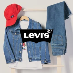 Cappellino rosso, giacca di jeans sopra una t-shirt bianca e jeans blu piegati appesi a un appendiabiti in legno su uno sfondo semplice.