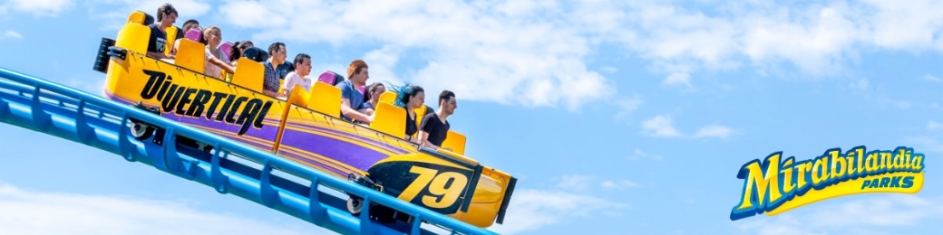Yellow and purple Divertical roller coaster car (79) with riders on a blue track against a blue sky, Mirabilandia Parks logo