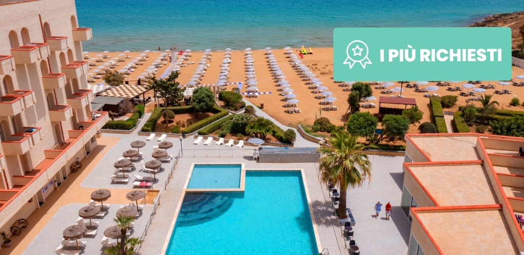Aerial view of a coastal resort with a blue hotel pool, sun loungers and parasols on a sandy beach by turquoise sea