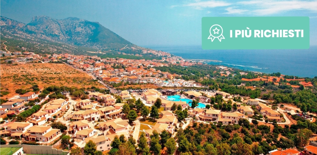 Aerial view of a Mediterranean coastal resort with terracotta-roof villas, pools, pine trees, mountains and sea, with an "I PIÙ RICHIESTI" badge