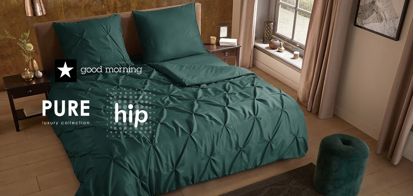 Set di biancheria da letto turchese con trama imbottita, due cuscini abbinati, comodino in legno, sgabello verde come accento e tappeto scuro a motivo in una stanza moderna.