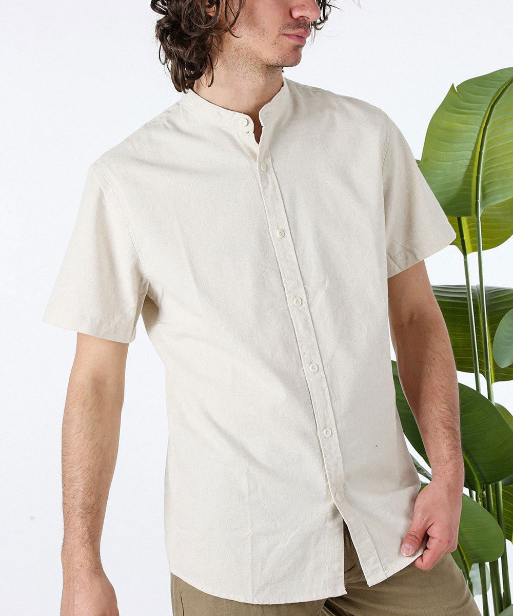 Person wearing cream short-sleeve mandarin-collar button-up shirt and khaki trousers, standing beside green tropical plant