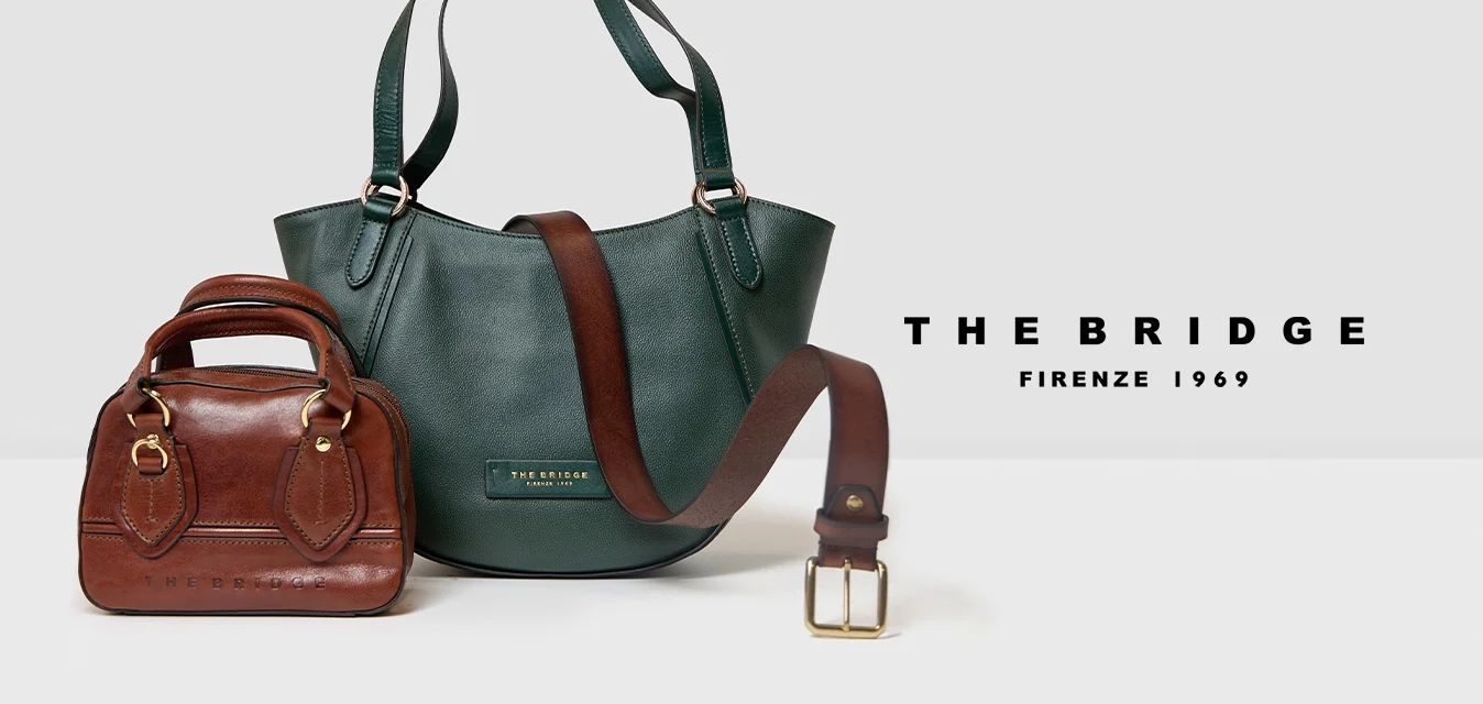 Piccola borsa a tracolla in pelle marrone e una borsa a spalla in pelle verde più grande, con una cintura in pelle marrone poggiata sopra, su una superficie bianca.