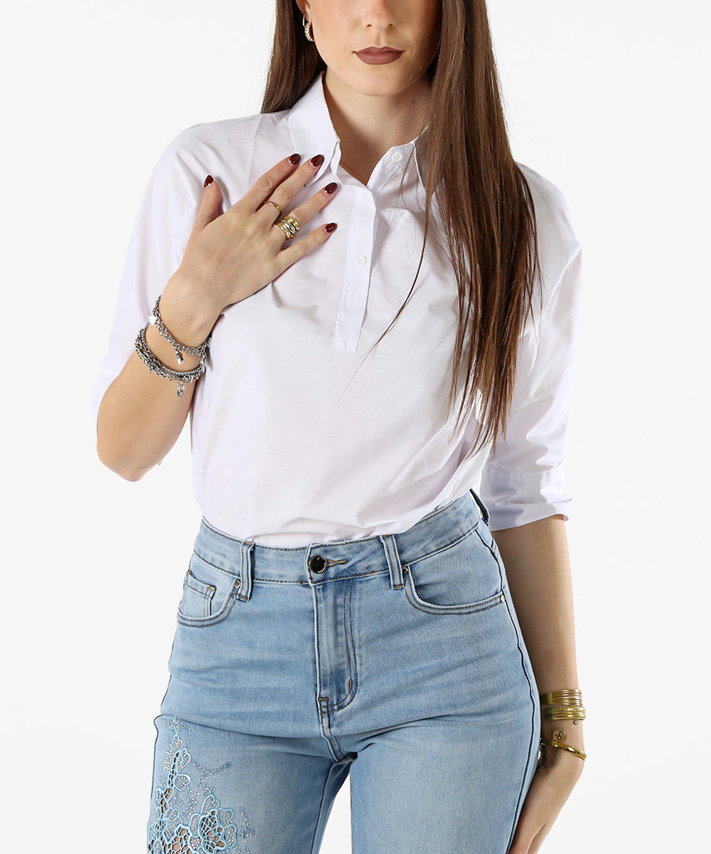 Woman in white polo shirt tucked into high-waisted light blue jeans with embroidery, bracelets and rings