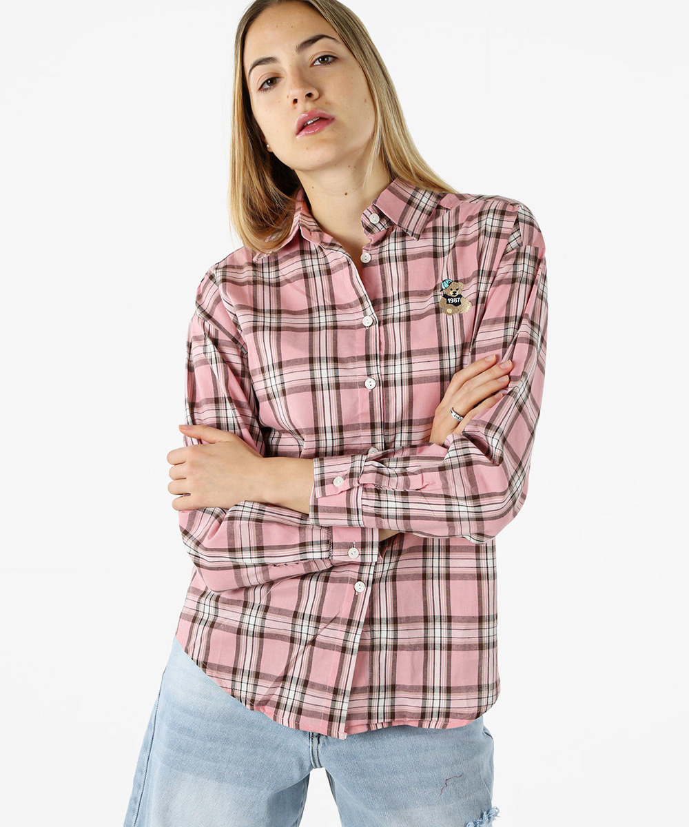 Woman modelling a pink plaid long-sleeve button-up shirt with embroidered patch, paired with light denim jeans