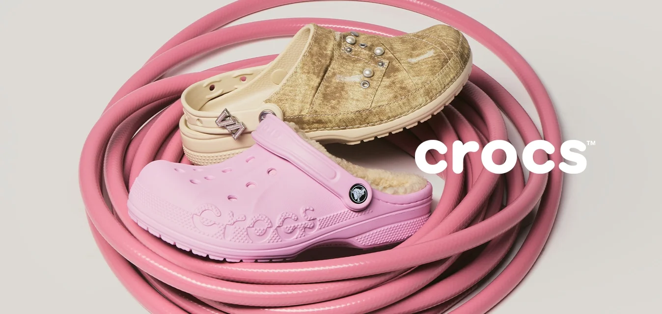 Tubo da giardino rosa arrotolato con tre scarpe di gomma usurate in tonalità beige, marrone chiaro e rosa chiaro posizionate sopra, su uno sfondo semplice.