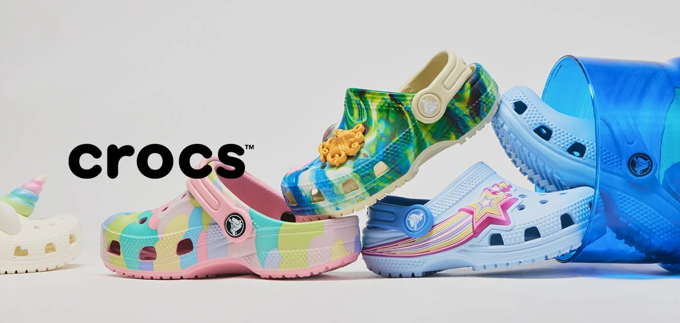 Cinque scarpe Crocs colorate disposte in un gioco di equilibrio, con due all'interno di un secchio traslucido blu ribaltato, su sfondo bianco.