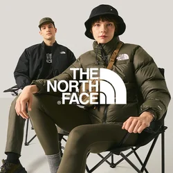 Due giovani seduti su sedie pieghevoli contro uno sfondo chiaro e semplice, uno dei quali indossa un cappello a secchiello nero e una giacca imbottita.