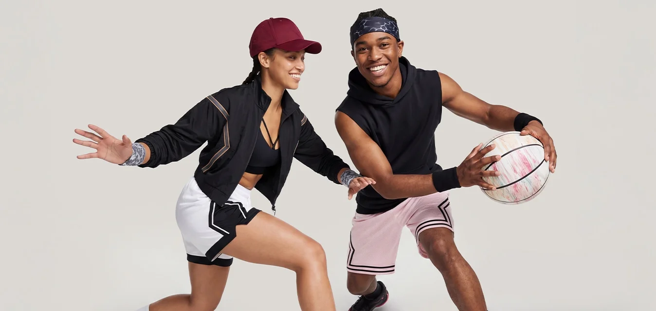 Uomo e donna che giocano a basket, uomo che palleggia, donna in posizione difensiva, entrambi indossano abbigliamento sportivo e scarpe da ginnastica.