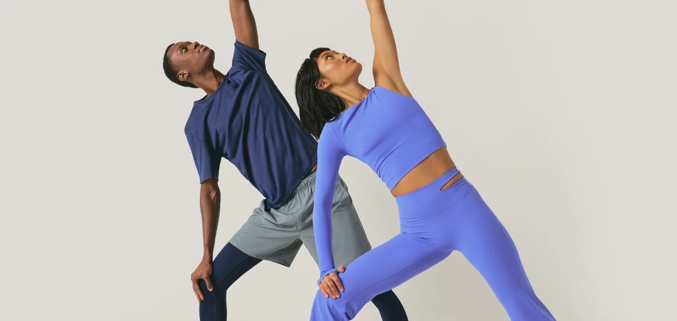 Due persone in abbigliamento sportivo che eseguono un allungamento laterale di yoga, con un braccio che si estende verso l'alto e l'altro che tocca la gamba.