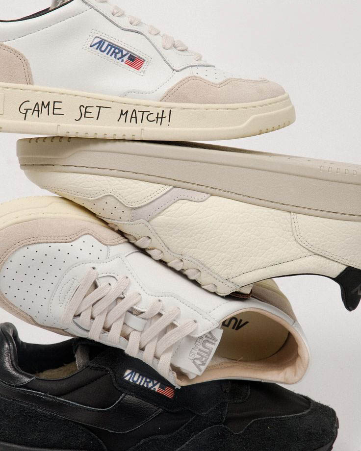 Stacked Autry leather sneakers in white, cream and black, close-up showing handwritten "GAME SET MATCH!" on the cream sole