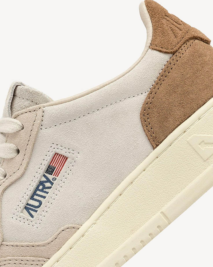 Close-up of beige suede Autry trainer with brown suede heel patch, cream rubber sole and US flag logo