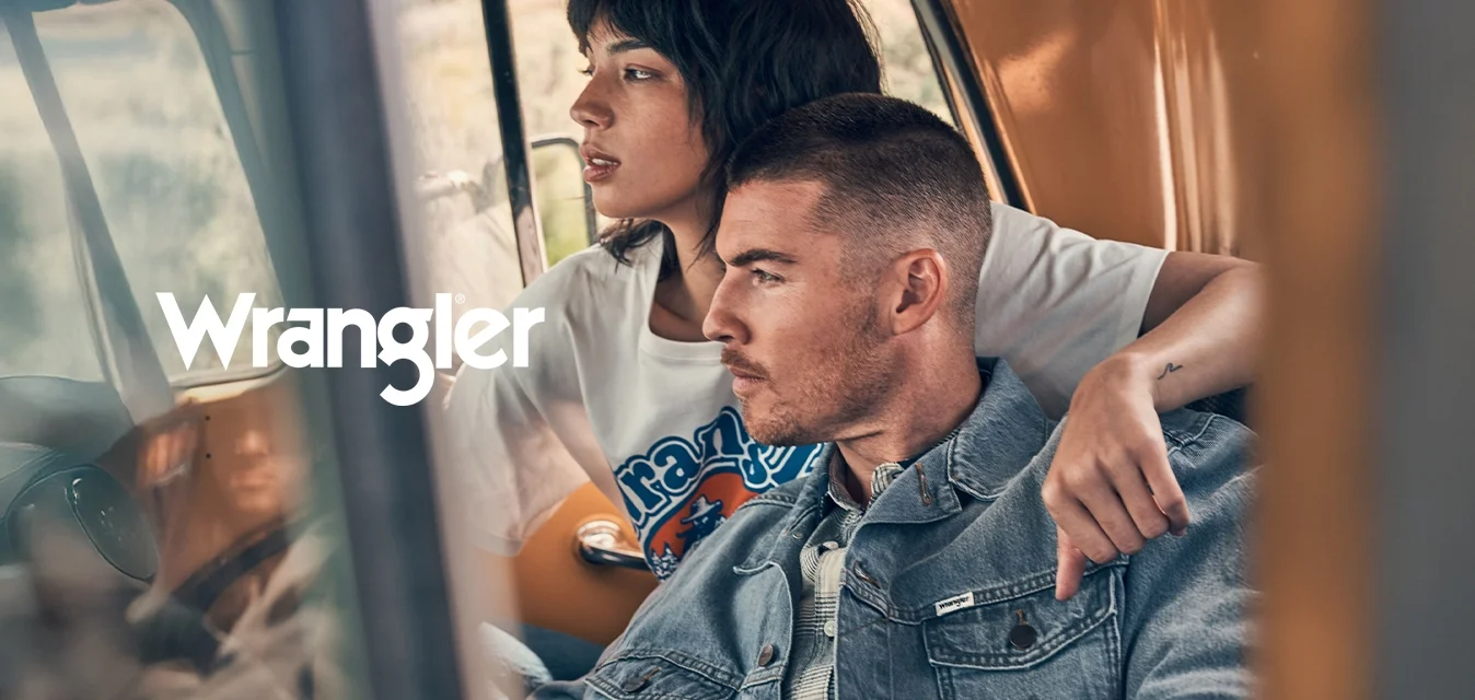 Giovane uomo con giacca di jeans e donna con t-shirt grafica seduti vicini in auto, entrambi guardano intensamente fuori dal finestrino.