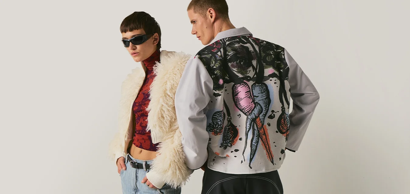 Due modelli posano; uno indossa occhiali da sole, una giacca pelosa e jeans, l'altro mostra una giacca dipinta con un'illustrazione colorata di carote sul retro.