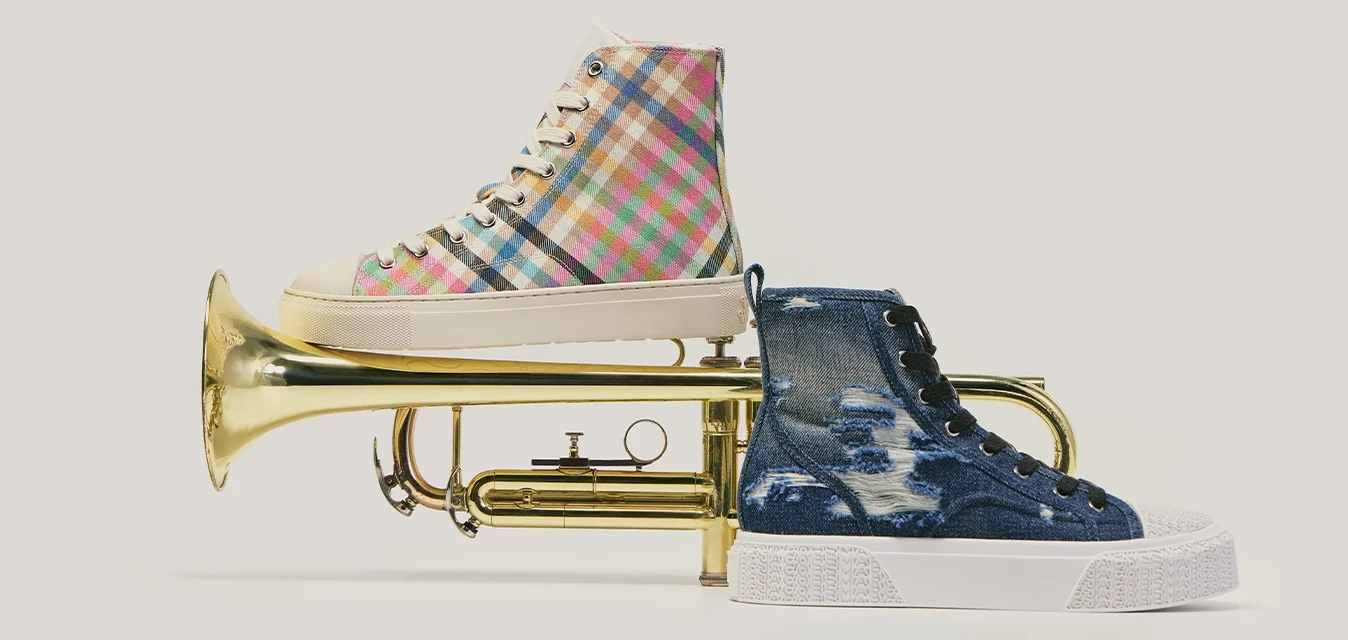 Tromba in ottone con una sneaker blu sul bocchino e una sneaker a quadri multicolore bilanciata sulla campana.