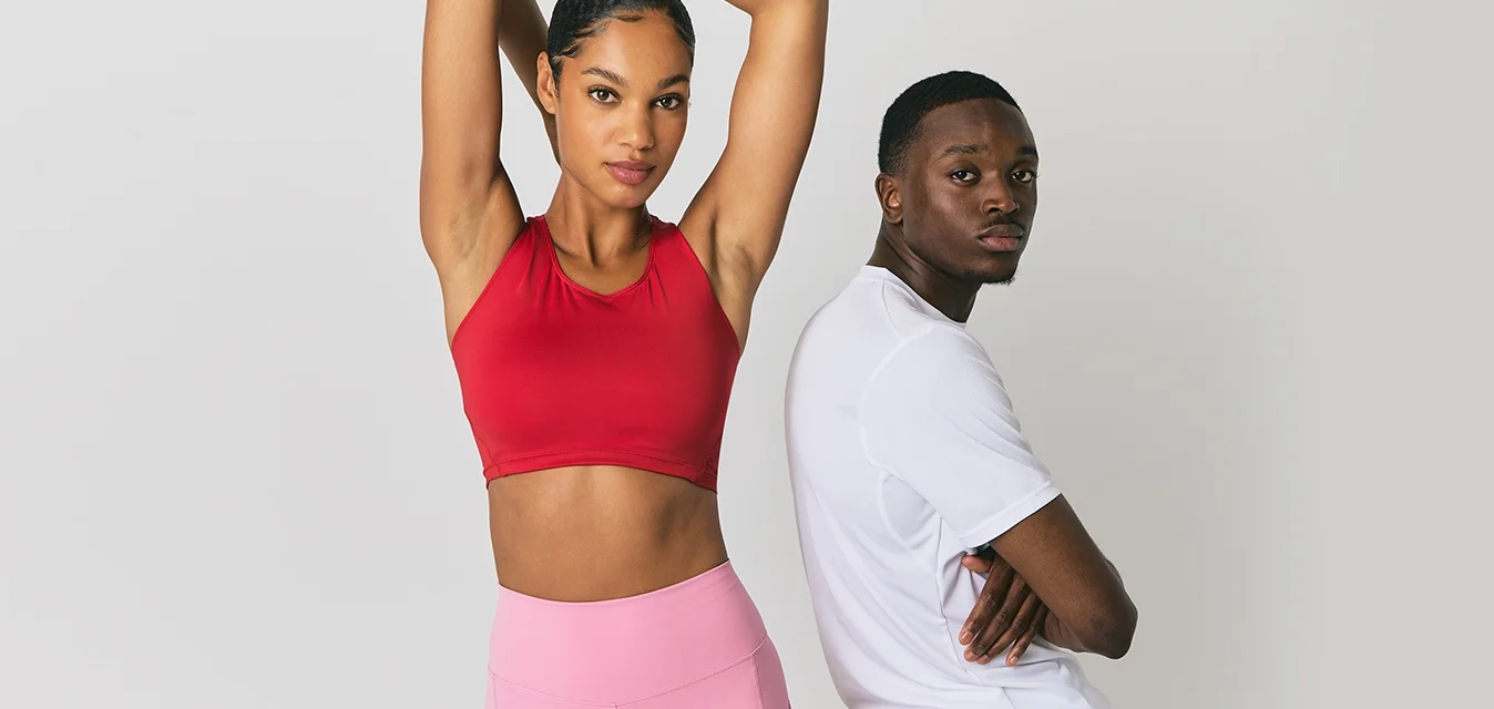 Top corto sportivo rosso, pantaloni corti rosa a vita alta su una persona; maglietta sportiva bianca con pantaloni corti azzurri chiari su un'altra, su uno sfondo in pelle marrone scuro.