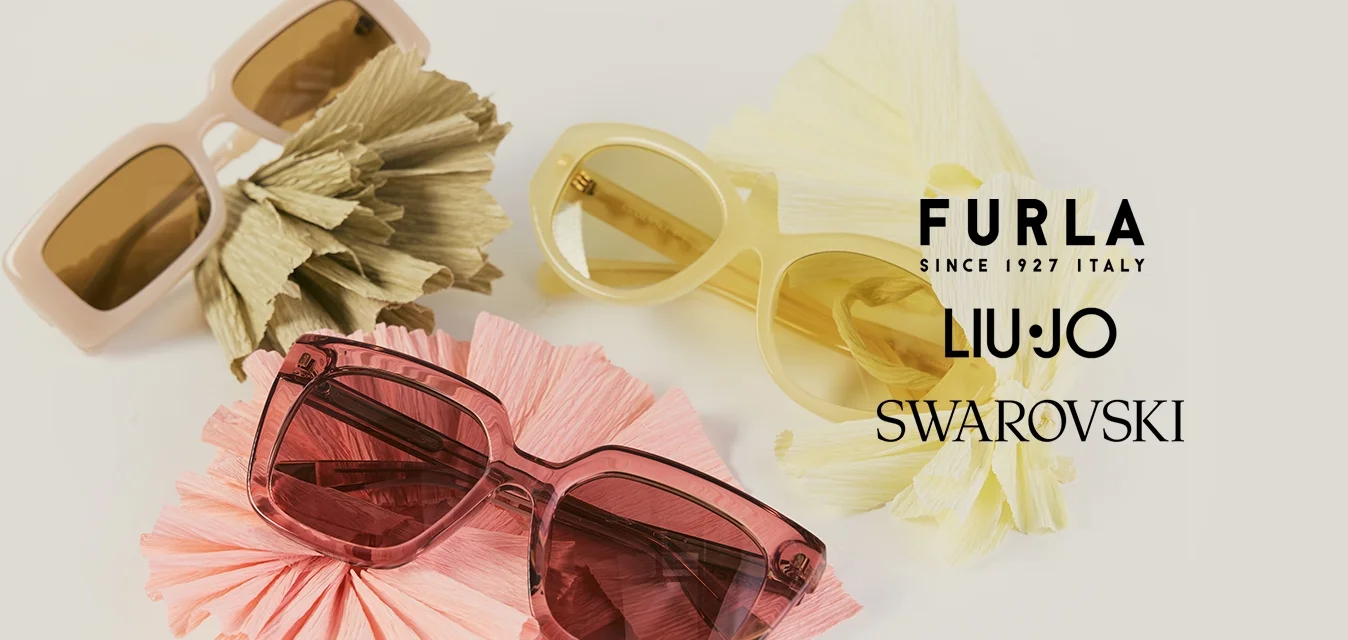 Tre paia di occhiali da sole beige, giallo e rosa, ciascuno appoggiato su un fiore di carta stropicciata abbinato su uno sfondo chiaro.