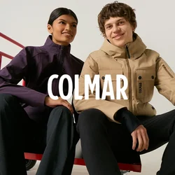 Due giovani adulti siedono su un carrello rosso, indossano giacche casual da esterno e pantaloni neri, sorridendo davanti a uno sfondo semplice.