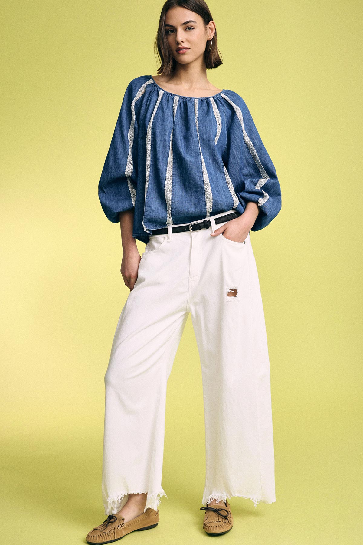 Model in blue striped peasant blouse, wide-leg frayed white jeans and tan moccasins against pale yellow background