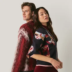 Uomo e donna in piedi schiena contro schiena davanti a uno sfondo uniforme, indossando maglioni con motivi e guardando in direzioni opposte.