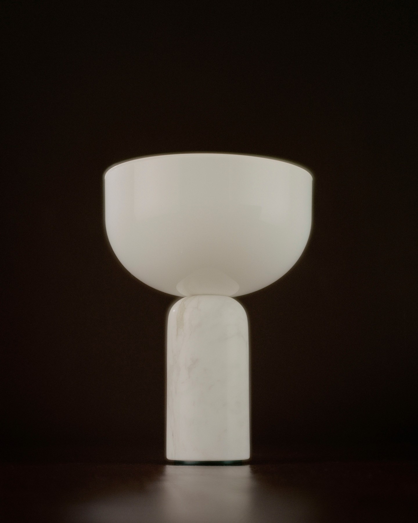 Minimalist white alabaster bowl atop cylindrical marble pedestal, modern decorative table sculpture against dark background