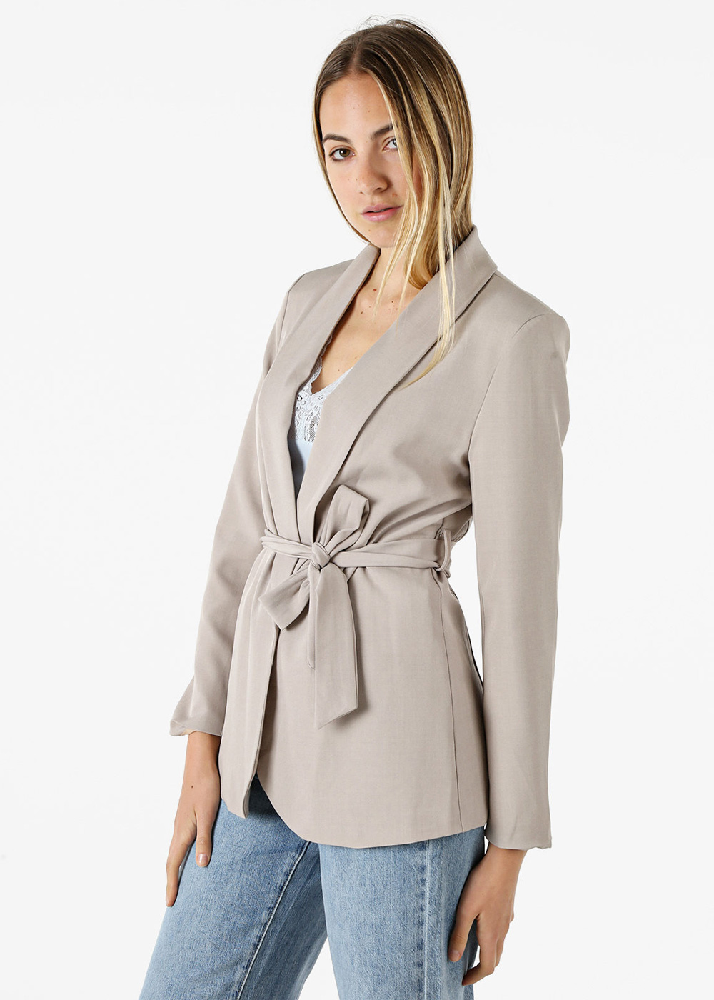 Woman modelling beige belted blazer over white lace camisole and blue jeans in studio