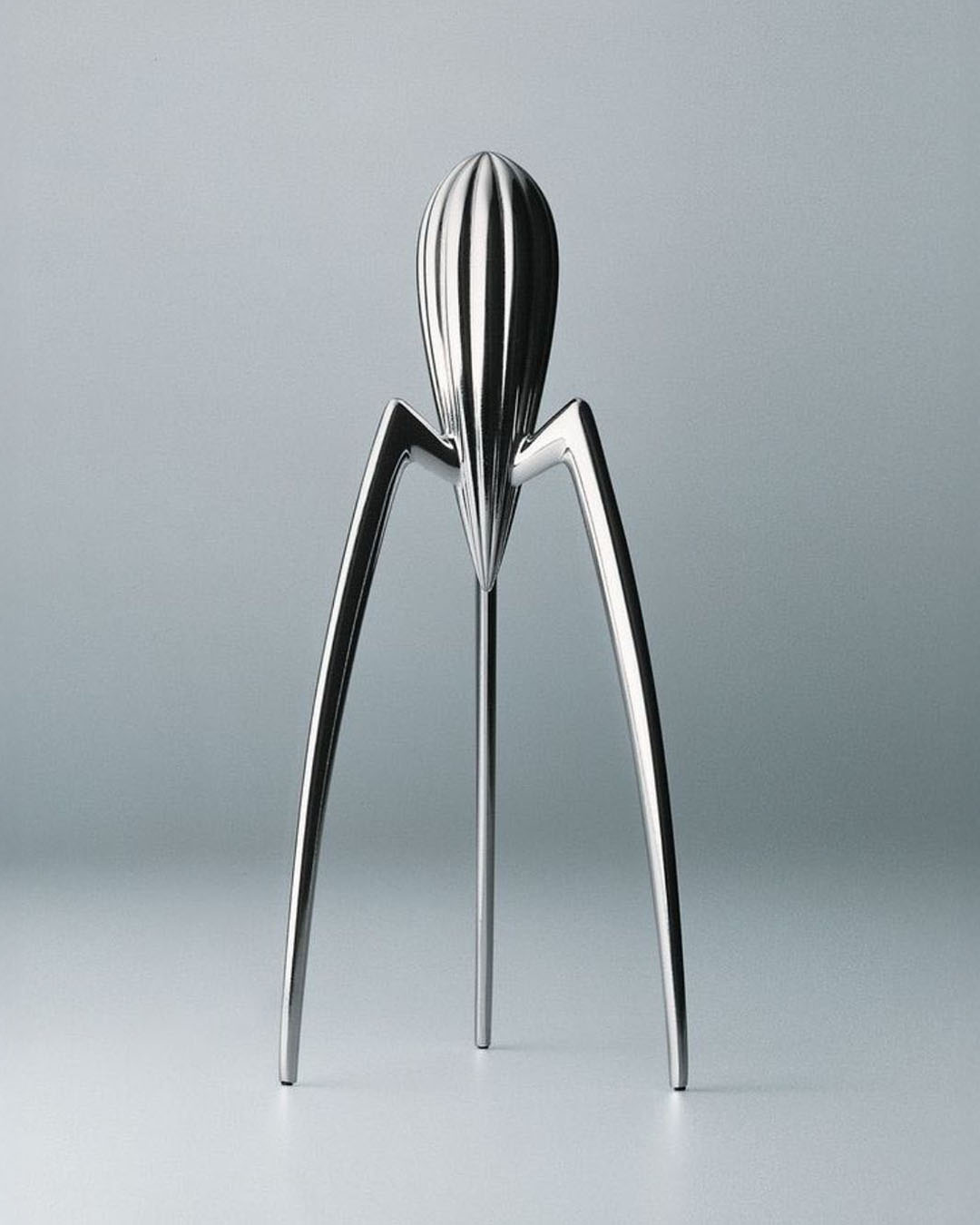 Polished stainless-steel Alessi Juicy Salif citrus juicer with three curved legs on pale grey background