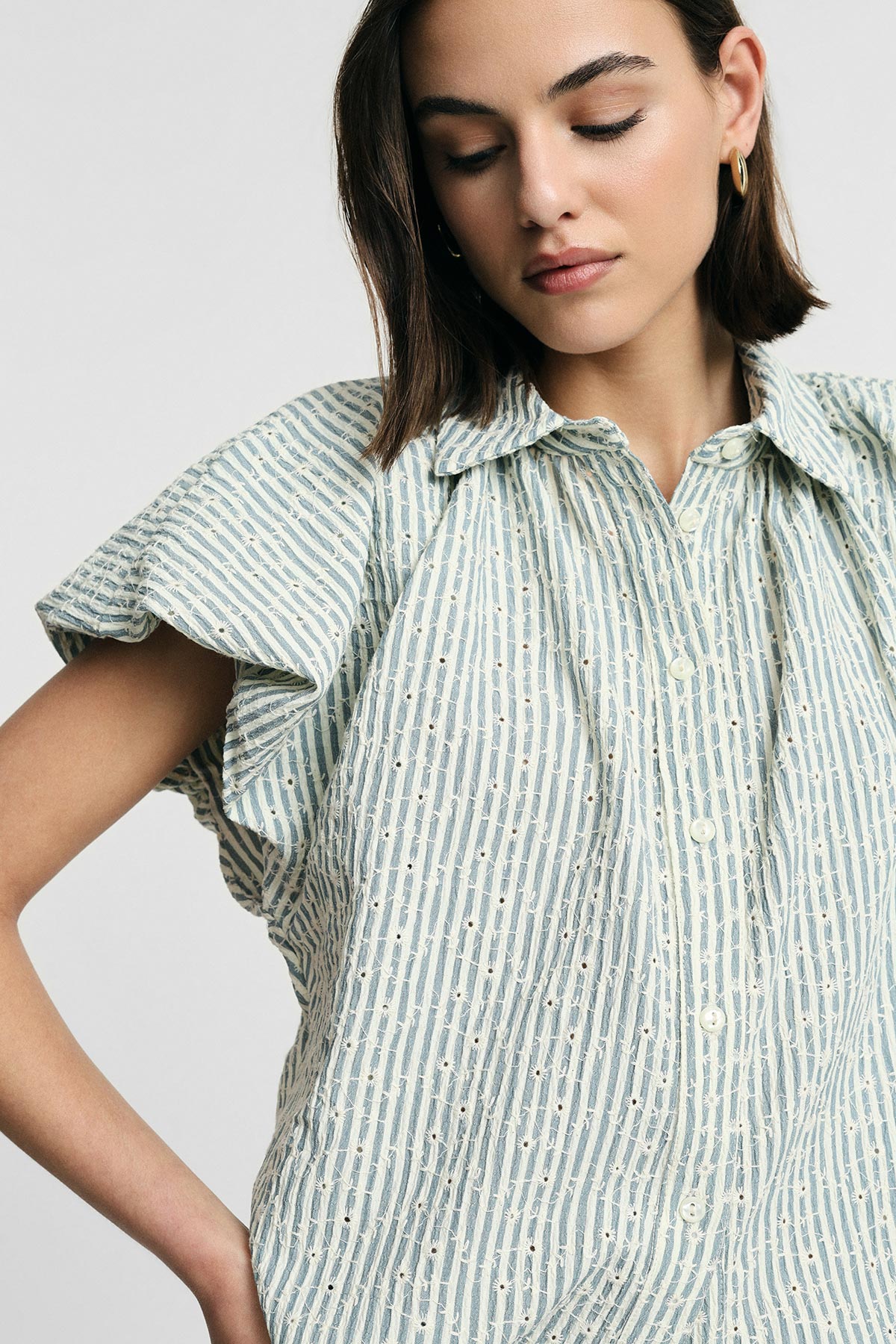 Woman wearing light-blue striped button-up women's blouse with short ruffle sleeves and gold hoop earring