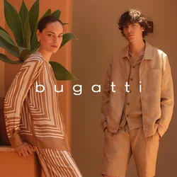 Due persone con abiti in tonalità neutre sono in piedi su scalini in terracotta vicino a piante in vaso, con colline rocciose e cielo nuvoloso sullo sfondo.