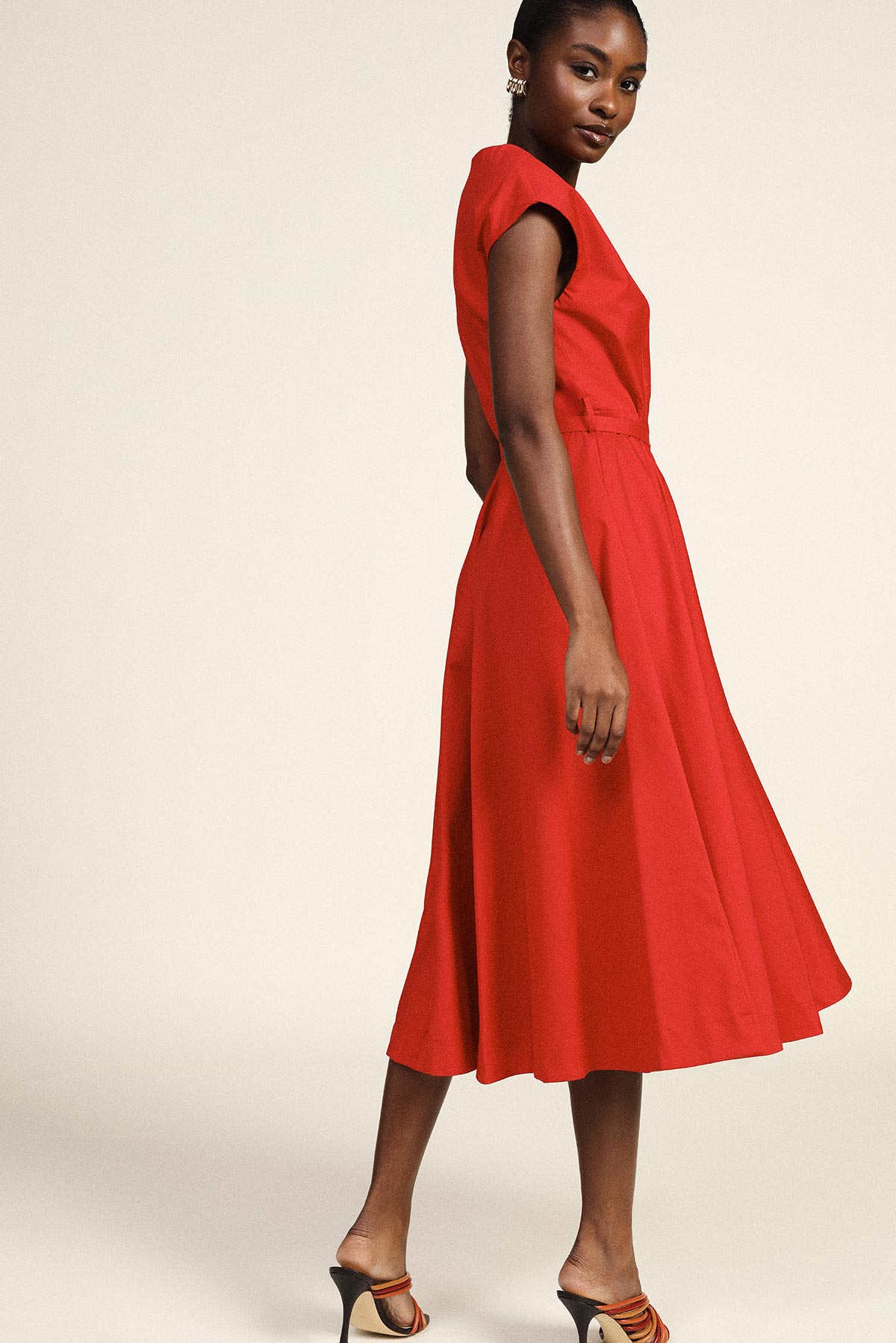 Black female model in a red cap-sleeve midi dress with flared skirt and heels, posing against a neutral background