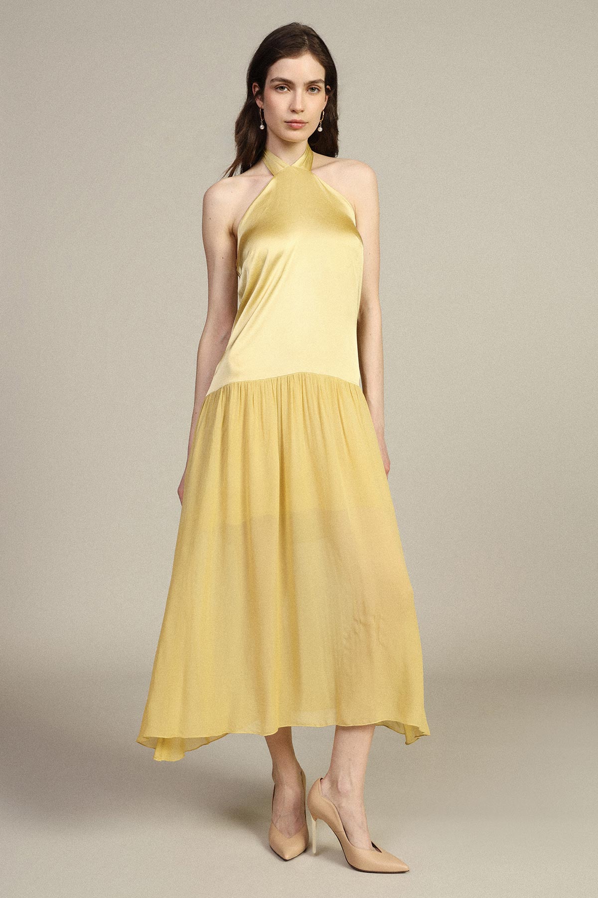 Model wearing yellow halter midi dress and nude heels against a neutral background