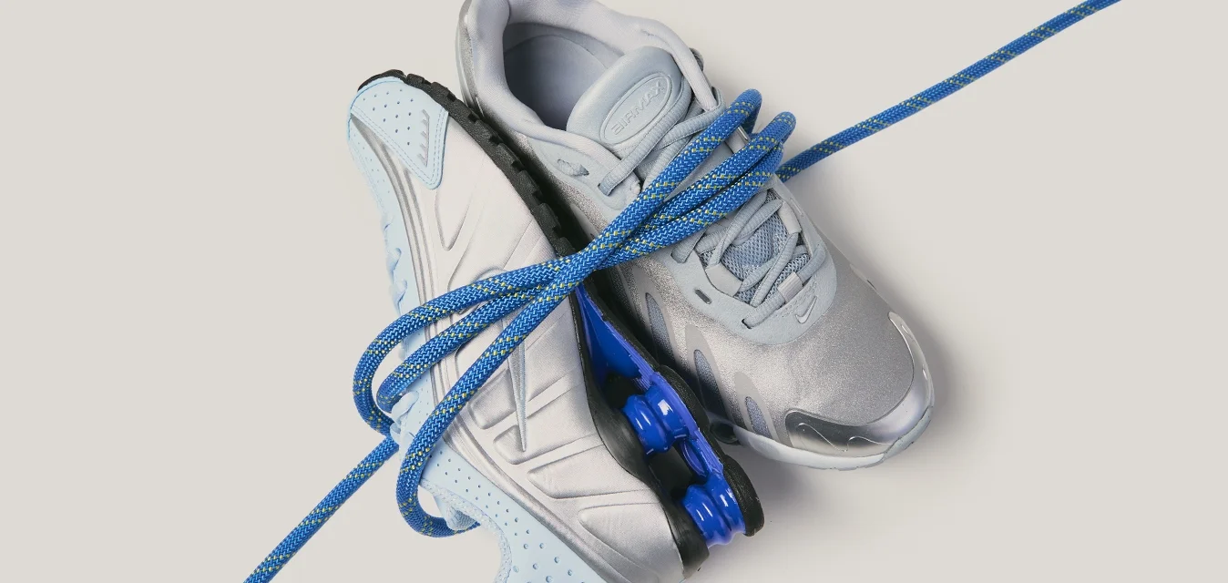 Coppia di scarpe sportive grigio chiaro e blu intrecciate da una corda blu su uno sfondo chiaro.