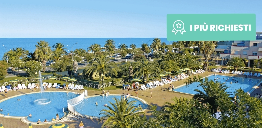 Aerial view of a beachfront resort with palm trees, two large swimming pools, sunloungers and the sea beyond