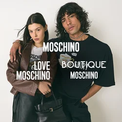 Giovane con capelli ricci in una maglietta nera con grafica ha un braccio attorno a una donna che indossa una giacca marrone, una gonna nera e tiene una borsa nera.