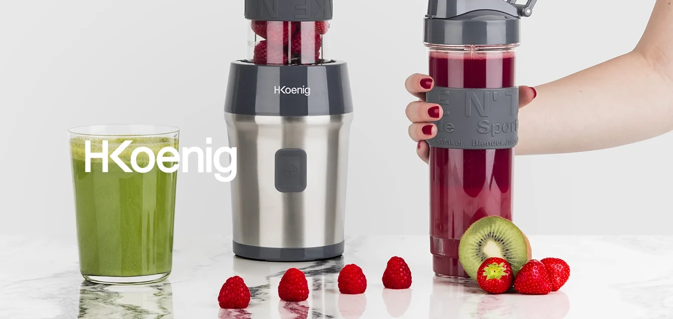 Frullatore con base in acciaio inox, parte superiore trasparente riempita di lamponi, abbinato a una borraccia sportiva grigio scuro, smoothie verdi e rossi.