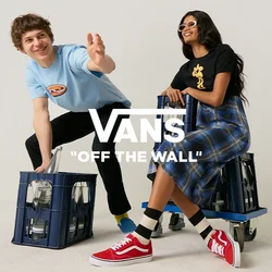 Un giovane uomo si protende in avanti mentre si accovaccia accanto a una cassa, e una giovane donna con occhiali da sole è seduta su una cassa con ruote in uno studio semplice.