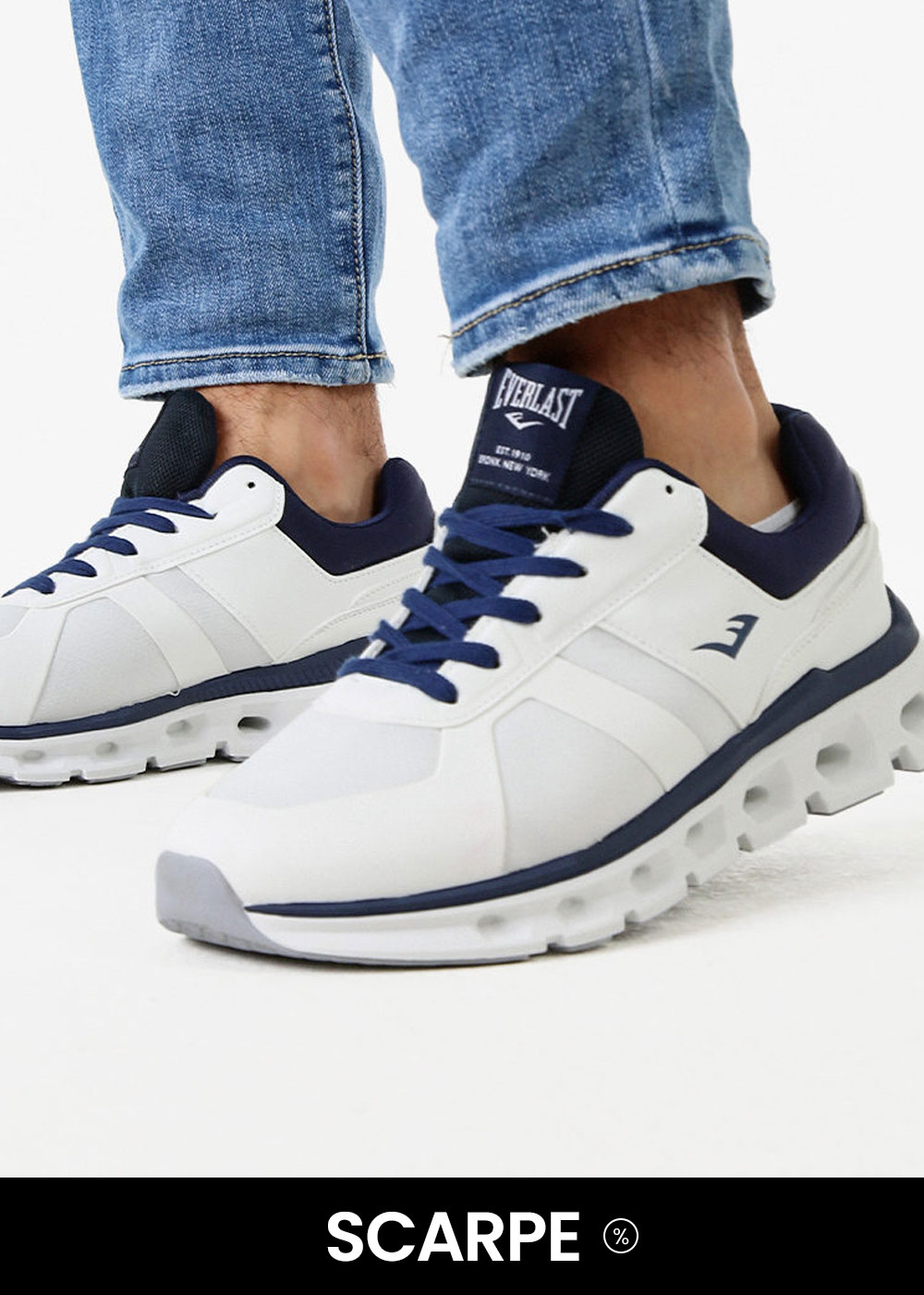 Pair of white and navy Everlast trainers on feet wearing rolled blue jeans, angled studio shot