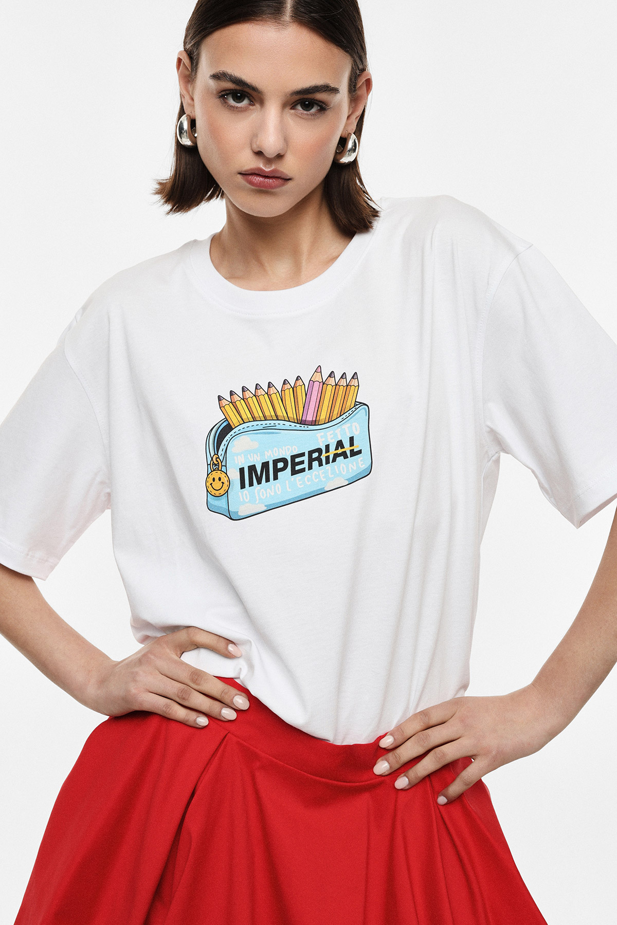 Young woman wearing a white graphic T‑shirt with a colourful pencil‑case 'IMPERIAL' print, red skirt, hands on hips
