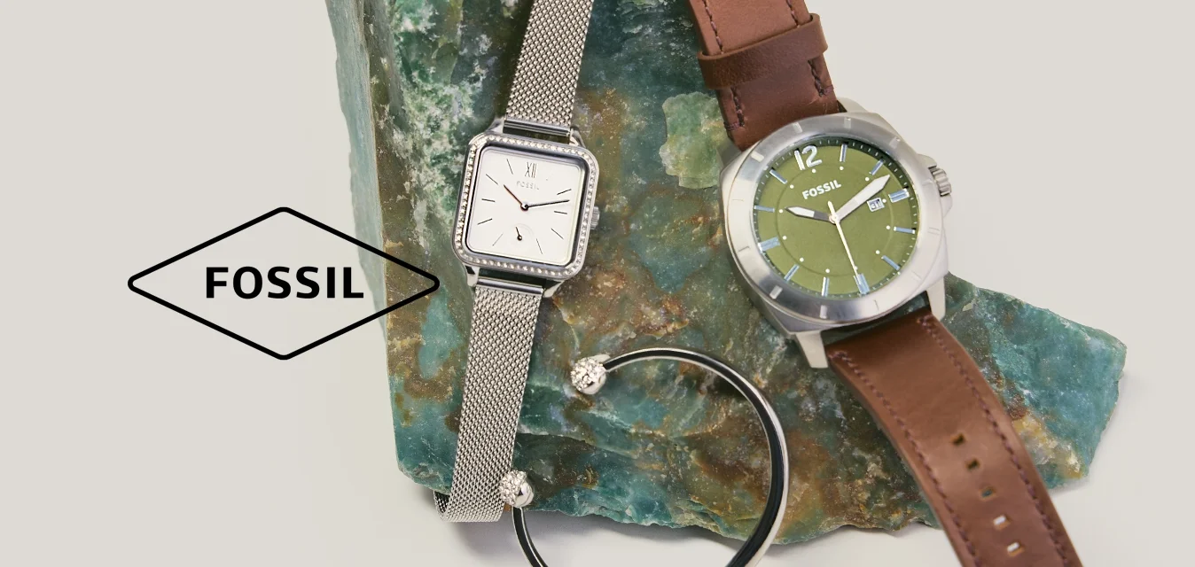 Due orologi da polso—uno argento con cinturino a rete, uno con quadrante verde e cinturino in pelle marrone—e un braccialetto nero su una pietra verde grezza.