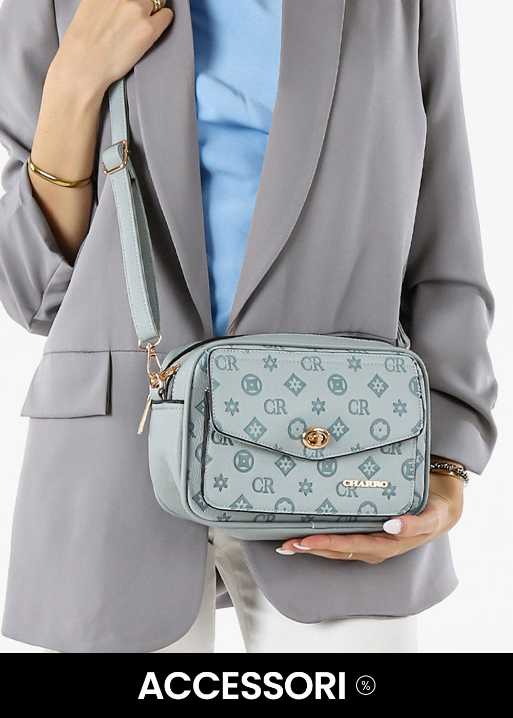 Person holding light blue monogram crossbody bag with gold clasp and adjustable strap, styled with grey blazer