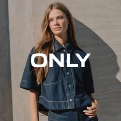 Giovane donna con capelli lunghi in piedi contro un muro di cemento, indossando una camicia a maniche corte in denim scuro e jeans a vita alta abbinati.