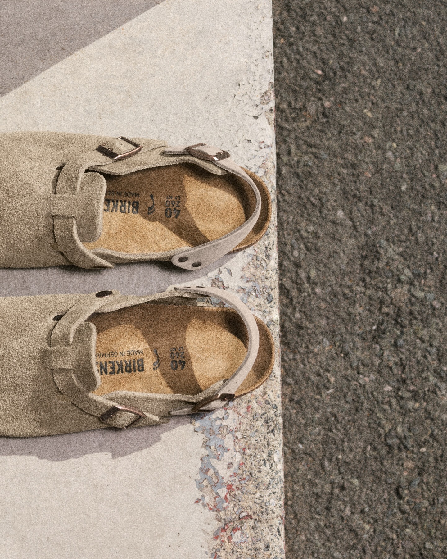 Beige suede Birkenstock sandals with buckles, top view on a concrete ledge beside asphalt