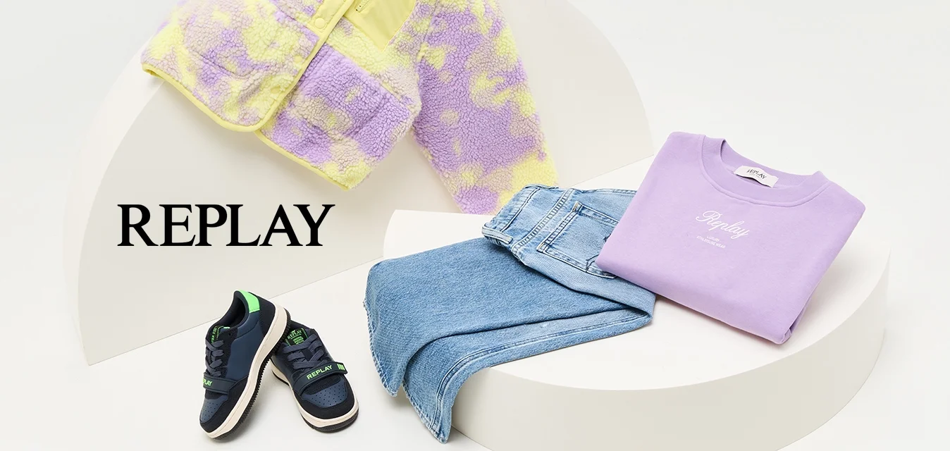 Giacca pelosa viola e gialla, felpa lavanda, jeans blu e sneakers navy con dettagli verdi, disposti su un'esposizione curva bianca.