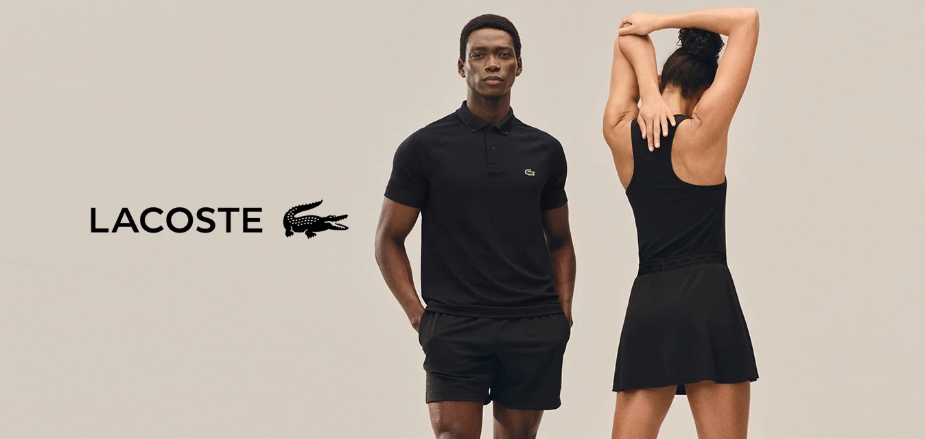 Due persone vestite con abbigliamento sportivo nero stanno davanti a uno sfondo uniforme; una è rivolta in avanti con le mani nelle tasche, l'altra allunga le braccia sopra la testa.