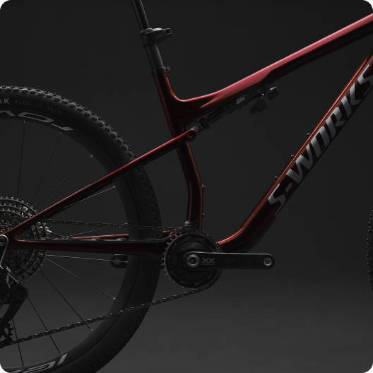 Close-up of red S‑Works full-suspension mountain bike frame, crankset, rear wheel and chain against a dark studio background