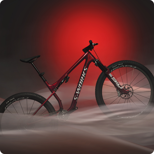 Red S-Works full-suspension mountain bike with carbon frame displayed in red spotlight and low-lying fog
