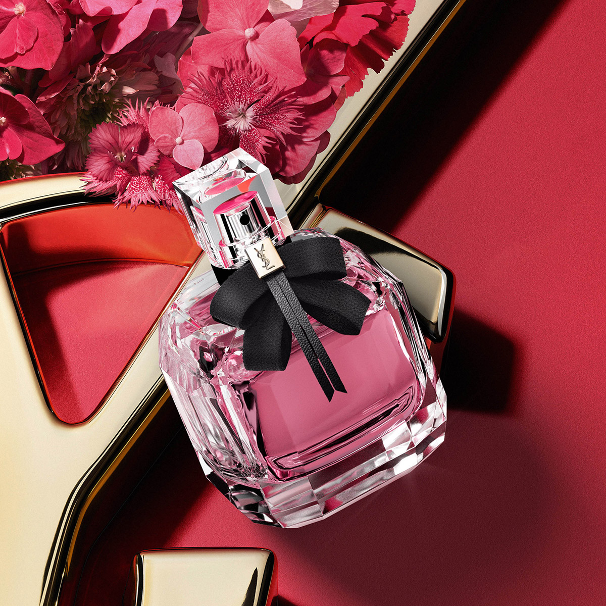 Un flacone di profumo Mon Paris su un logo YSL dorato con fiori rosa.